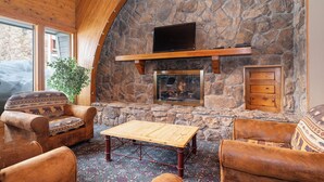 A stone fireplace with a flat-screen TV above it, surrounded by leather armchairs and a wooden coffee table. - Silverado II Unit 334 Great views clubhouse amenities bedding for 2 couples (Winter Park)