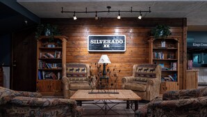 A cozy room with a wooden wall, two armchairs, a coffee table, and bookshelves filled with books. - Silverado II Unit 334 Great views clubhouse amenities bedding for 2 couples (Winter Park)