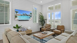 Amplia sala de estar con televisor grande, asientos cómodos y vista a una piscina a través de grandes ventanales.