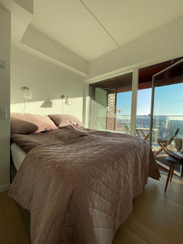A bedroom with a large bed, a balcony with a view of the city, and a modern design.