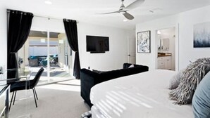 Une chambre d’hôtel moderne dotée d’un grand lit, d’un ventilateur de plafond, d’un téléviseur à écran plat et offrant une vue sur l’espace extérieur grâce à des portes vitrées.
