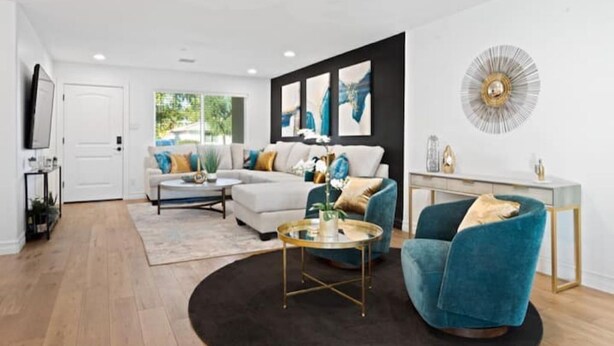 Un salon moderne avec un canapé, une table basse et un fauteuil, un téléviseur et des œuvres d’art accrochées au mur.