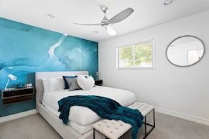 Ein modernes Schlafzimmer mit Bett, Deckenventilator, Nachttisch, Fenster und Spiegel an der Wand.