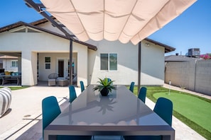 Eine moderne Terrasse mit einem Glastisch, blauen Stühlen und einem großen Sonnenschirm.