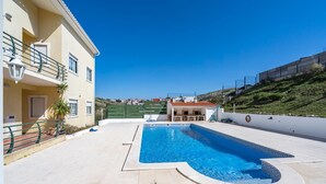 A swimming pool area with a pool, a building with a balcony, and a view of a hillside.