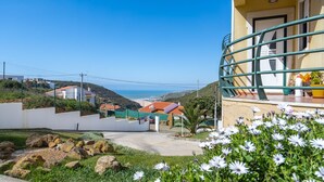 A residential building with a balcony, a view of the sea, and a garden with white flowers.