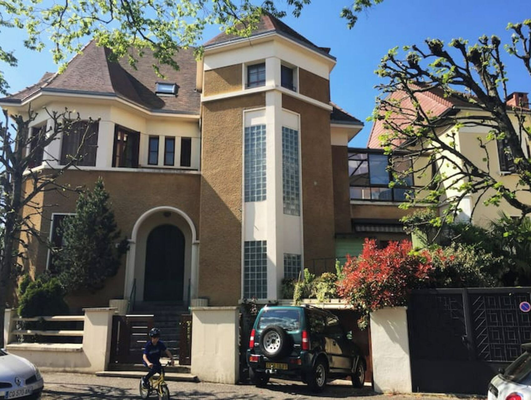 A two-story house with a prominent arched entrance, a garage, and a black SUV parked in front.