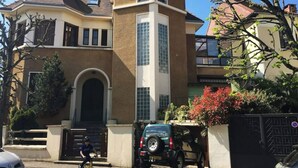 Ein zweistöckiges Haus mit einem markanten Bogenportal, einer Garage und einem schwarzen SUV davor.