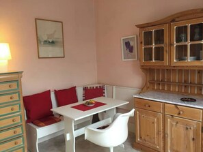 A cozy room with a white bench, a small table with a red placemat, wooden cabinets, and a wall-mounted lamp. - Studio on Lake Allier, 5mn City Center & Thermal Baths (Vichy)