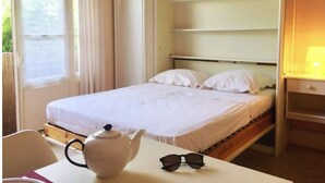 Ein Einzelbett mit Kopfteil, ein Nachttisch mit Lampe und ein Fenster mit Vorhängen.