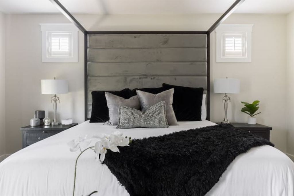 Ein Schlafzimmer mit einem großen Bett, zwei Nachttischen, einer schwarzen, flauschigen Decke und einer Topfpflanze.