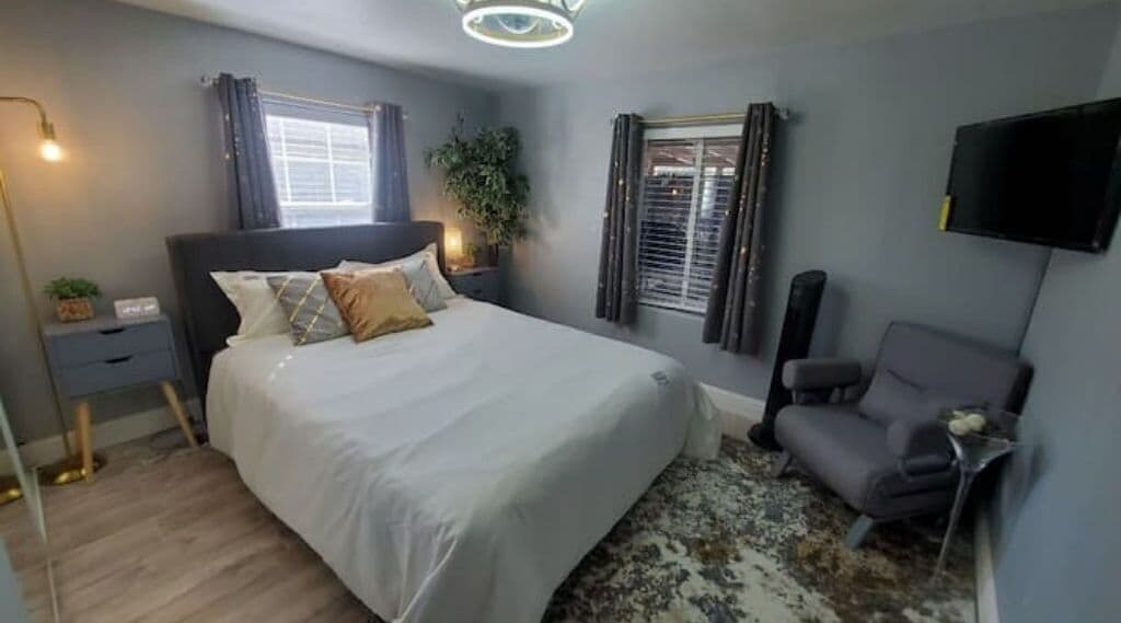 Une chambre à coucher comprenant un lit, une table de chevet, une lampe, une chaise et un téléviseur fixé au mur.