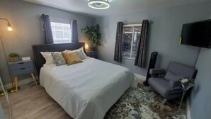 Ein Schlafzimmer mit Bett, Nachttisch, Lampe, Stuhl und einem an der Wand montierten Fernseher.
