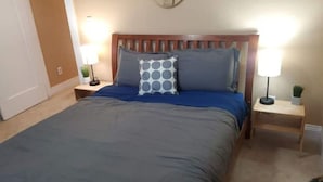 A bedroom with a wooden headboard, a blue bedspread, two bedside lamps, and a small plant on the nightstand. - The Modern Family Getaway (Oakland)