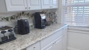 A kitchen with white cabinets, a granite countertop, a toaster, a coffee maker, and a window with blinds. - The Modern Family Getaway (Oakland)