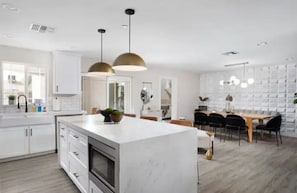 A modern kitchen with white cabinetry, a marble island, pendant lighting, and a dining area with a wooden table and chairs.