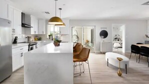 Une cuisine moderne avec des meubles blancs, un îlot central et un coin repas comprenant une table ronde et des chaises.