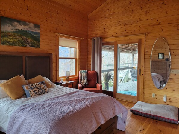 Quarto de cabana de madeira com uma cama, uma cadeira, uma janela e um espelho.