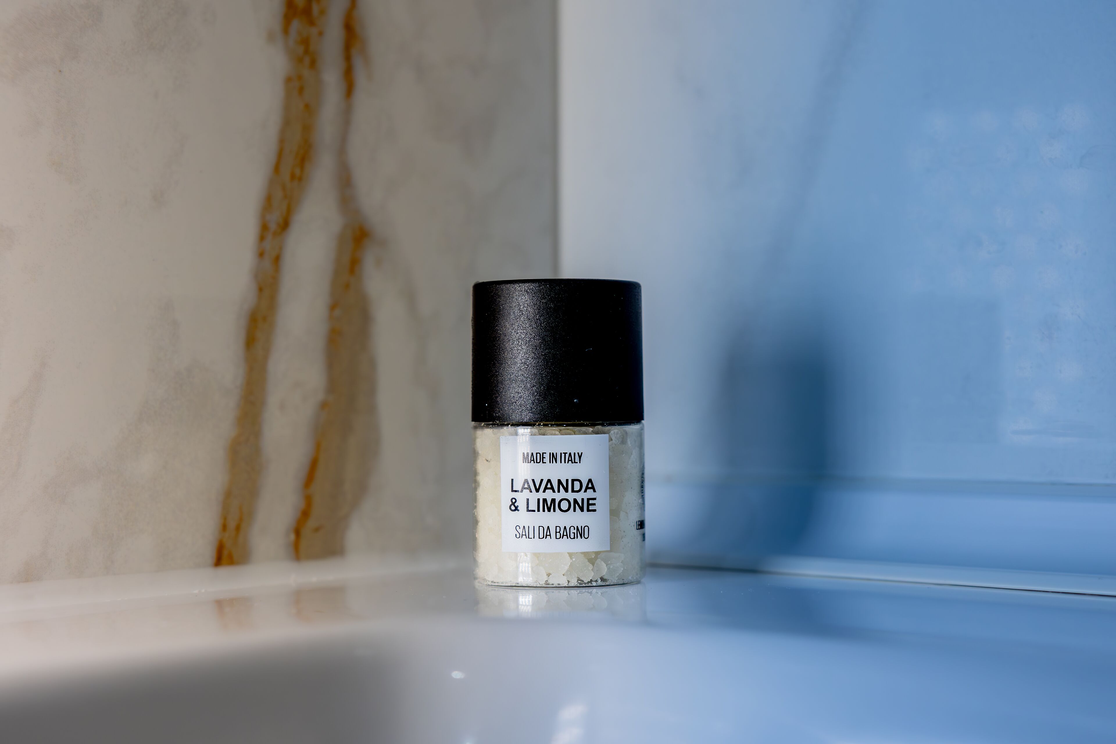 Pequeño recipiente de 'LAVANDA & LIMONE SALI DE BAÑO' sobre una superficie blanca.
