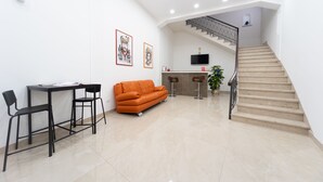 A modern living area with a sofa, chairs, a dining table, a staircase, and a TV mounted on the wall.