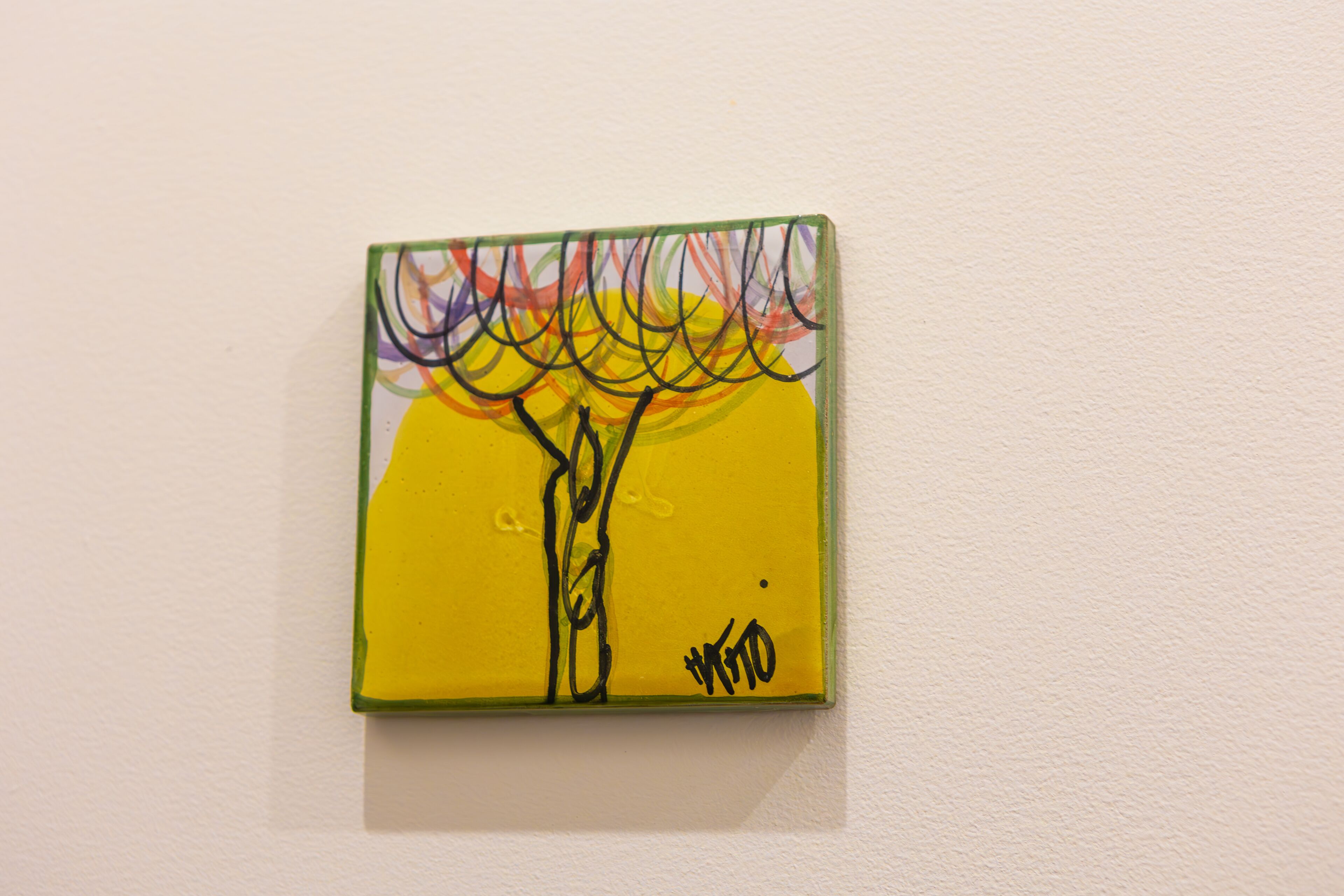 Ein kleines, gerahmtes Kunstwerk mit abstrakten Linien und einer Signatur auf gelbem Grund.