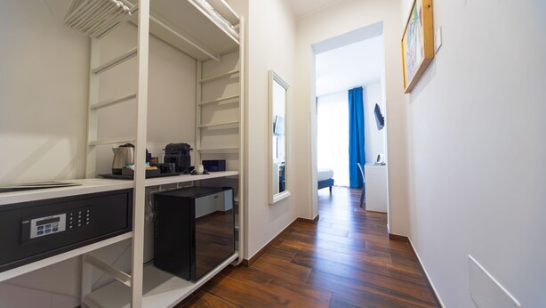 A modern hotel room with a walk-in closet, a compact kitchenette, and a view of the hallway.