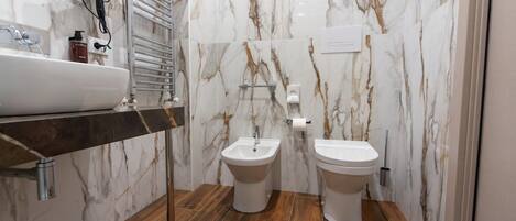 A modern bathroom with a marble backsplash, a wooden floor, a sink, a bidet, and a toilet.