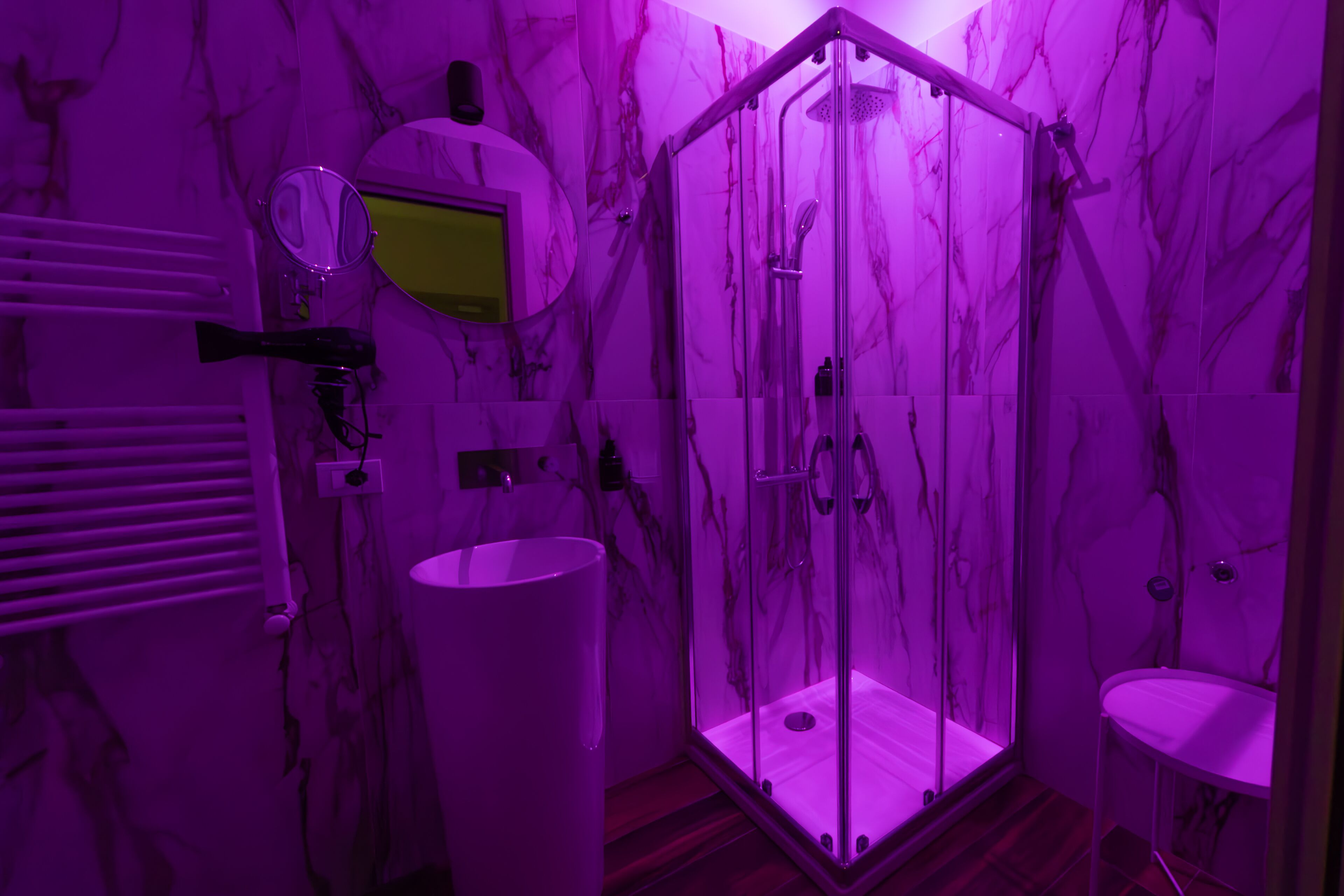 A bathroom with a glass-enclosed shower, a vanity with a mirror, and marble walls.
