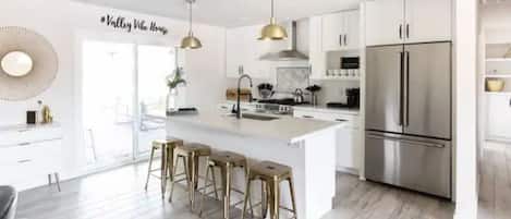 Una cocina moderna con una isla grande, electrodomésticos de acero inoxidable e iluminación colgante.
