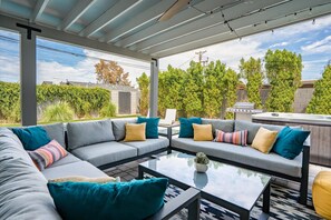 Relax in this outdoor living space with a sofa set, coffee table, and barbecue grill, surrounded by lush greenery and a scenic view.