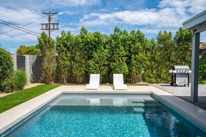 Relax by the rectangular pool surrounded by lush greenery and lounge chairs.