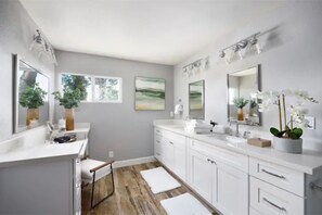 A modern bathroom with white cabinetry, a large mirror, and a wooden floor.