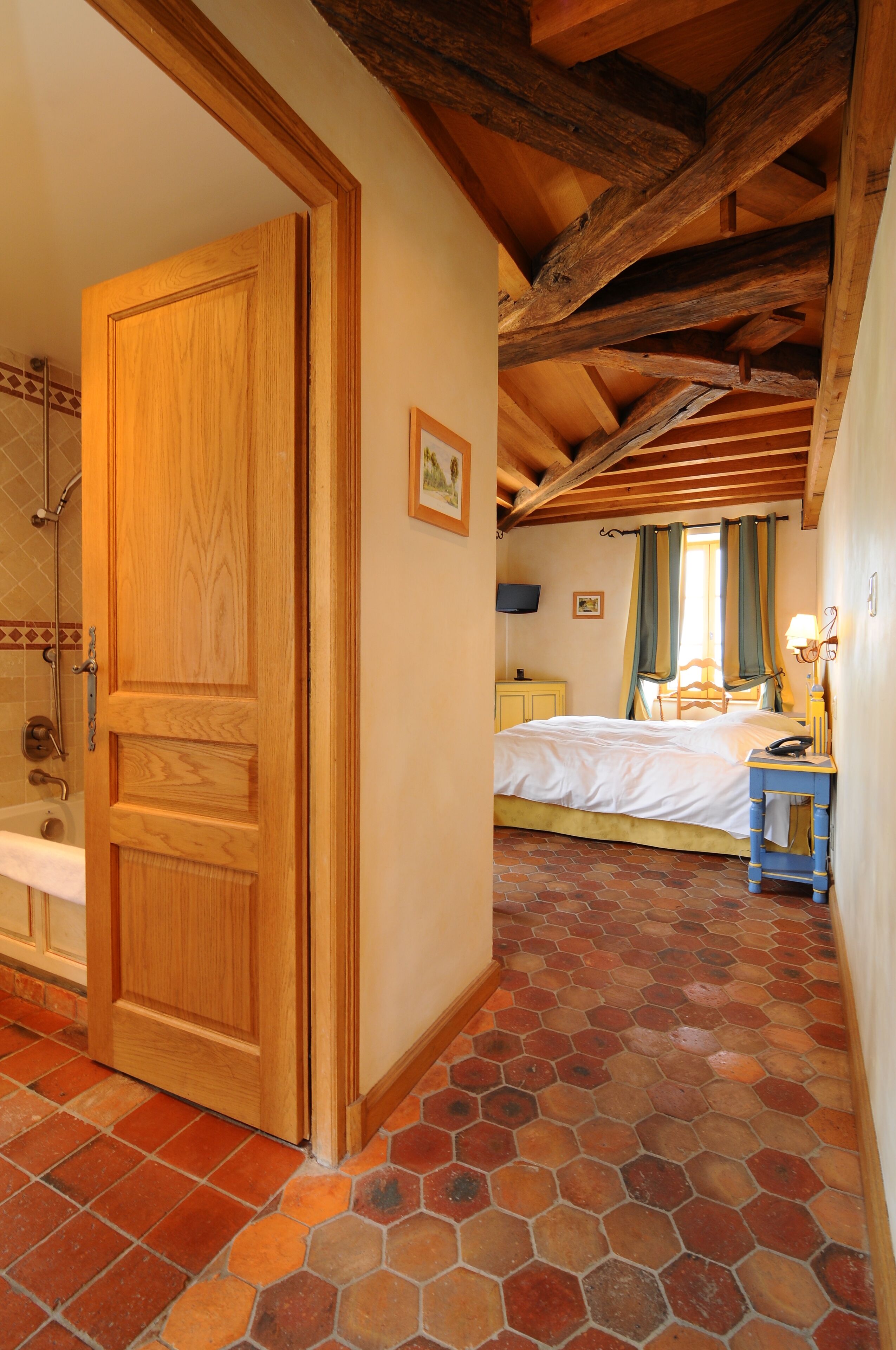 Quarto com porta de madeira, cama, mesa de cabeceira e banheiro com chuveiro.