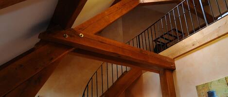 A staircase with wooden beams and a chandelier, leading to a room with a sofa and a lamp.