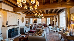 A spacious living room with a fireplace, multiple seating areas, and a high wooden ceiling with chandeliers.