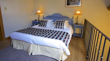 Cama bem arrumada com colcha listrada, duas luminárias de cabeceira e mesa de apoio com telefone.