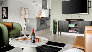 En moderne stue med et marmorbord, grøn sofa og et fladskærms TV på væggen.