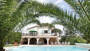 Ein zweistöckiges Haus mit Pool, umgeben von Palmen und einer Steinterrasse.