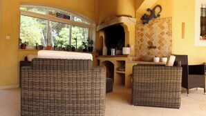 A cozy living area with wicker furniture, a fireplace, and a view of greenery through large windows. - Rental Residence Peylon with swimming pool terrace garden patio in a quiet area (Flayosc)