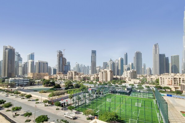 Un paysage urbain avec des immeubles modernes de grande hauteur, un terrain de sport verdoyant et un ciel dégagé.
