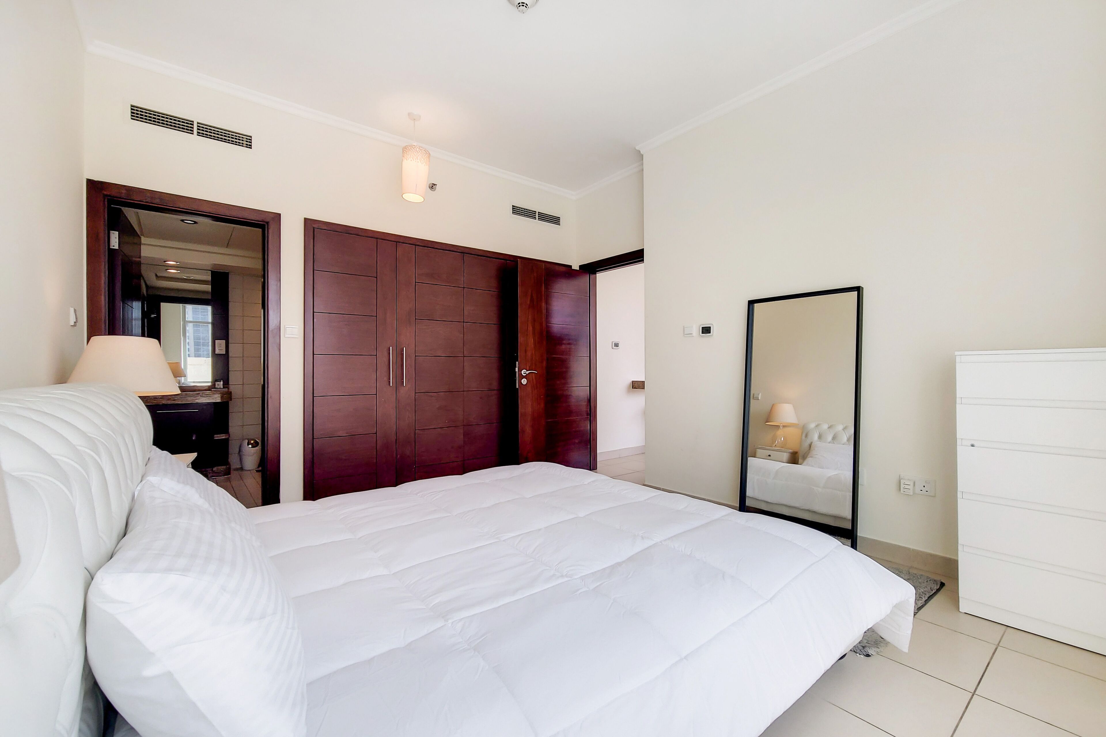 Um quarto com cama, guarda-roupa, espelho e mesa de cabeceira.