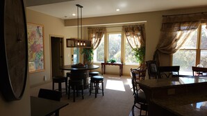 A dining area with a round table, bar stools, and a chandelier. There is a large window with curtains and a view of trees. - 0ver 7,000 Sq ft of tranquil relaxation  (Shawnee)