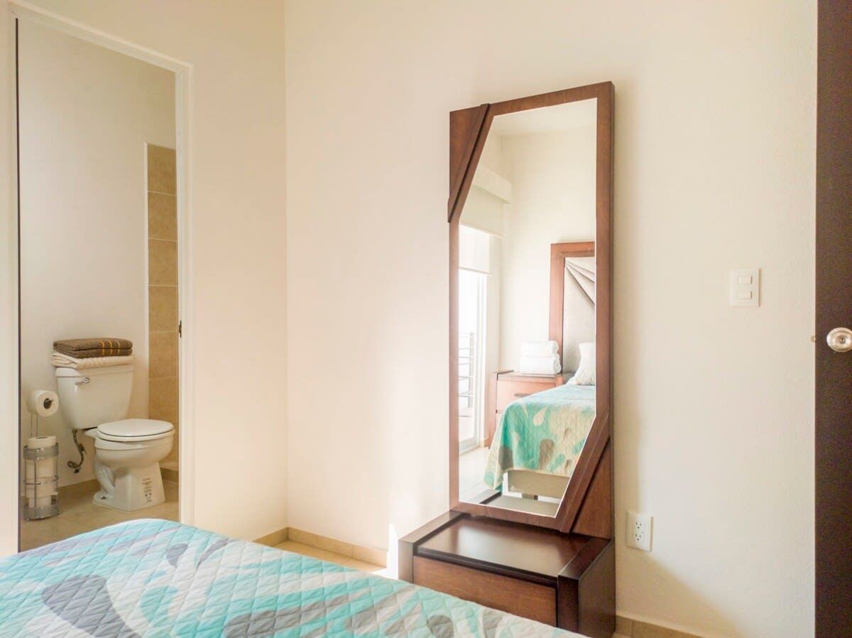 A bedroom with a bed, a dresser, a mirror, and a bathroom visible through an open door.