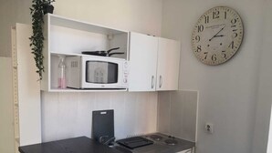A compact kitchenette with a microwave, a stove, and a sink. There is a clock on the wall and a small shelf with a plant. - Le Cosy Studio (Free parking) Whole apartment 15min from Luxembourg (Algrange)