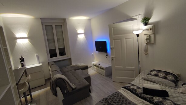 A modern bedroom with a sofa, a TV mounted on the wall, a bedside table, and a door. - Le Cosy Studio (Free parking) Whole apartment 15min from Luxembourg (Algrange)