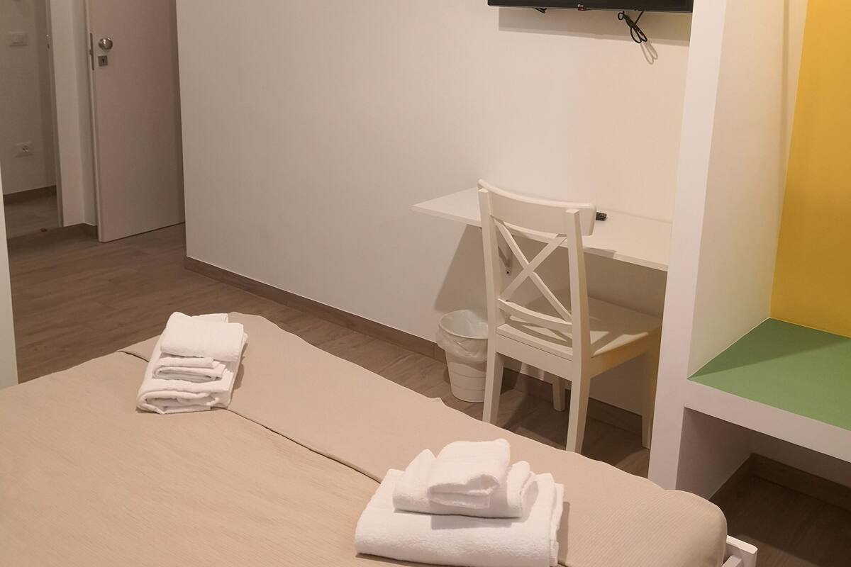 Ein Hotelzimmer mit Bett, Schreibtisch, Stuhl, Fernseher und Mülleimer.