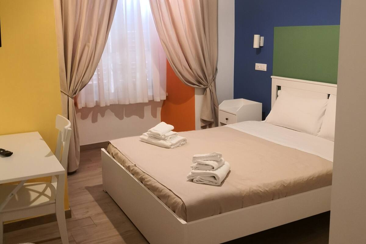 Ein Hotelzimmer mit Bett, Nachttisch, Stuhl, Schreibtisch und einem Fenster mit Vorhängen.