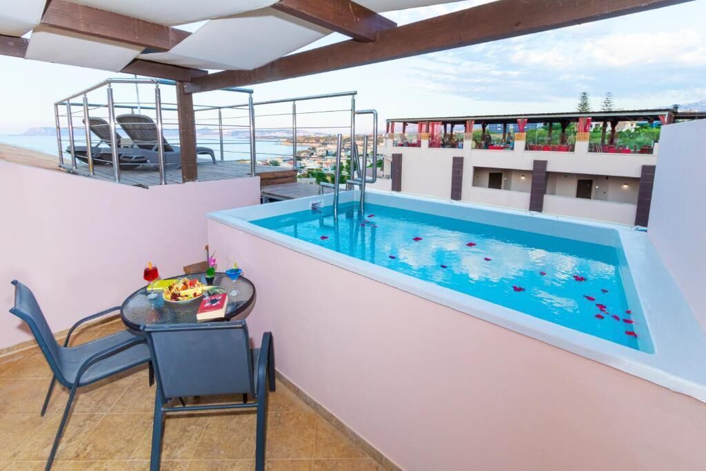 A rooftop pool with a glass table and chairs, a diving board, and a view of the cityscape.