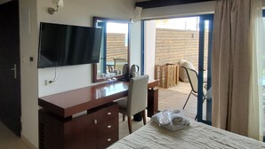 A hotel room with a bed, a desk, a chair, a television, and a large window. - Galini Private Pool Suites with Sea View (Chania)