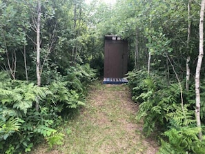 A pathway leading to a small, dark-colored structure surrounded by dense greenery and trees. - Pine Place with Dome (Woodridge)